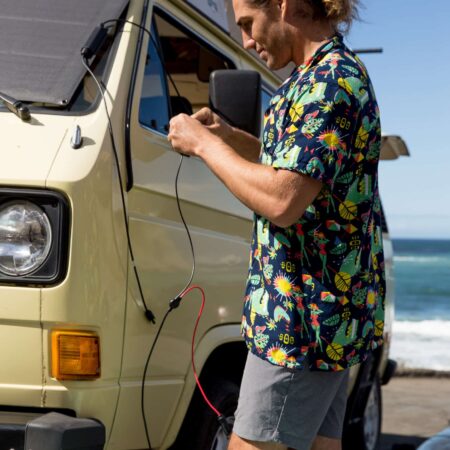 Charging a retro camper van with eco-friendly portable solar power system at the beach, promoting off-grid living and sustainable travel.