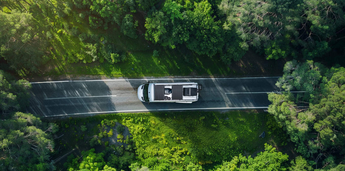 Eco-friendly off-grid camper van travelling through lush green forest on rural road in Ireland. Sustainable lifestyle, wilderness adventure, off-grid living, nature escape, van life, eco-tourism.